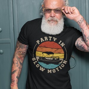 K&ouml;nnte beinhalten: Ein schwarzes T-Shirt mit einer Grafik im Vintage-Stil eines Bootes auf dem Wasser mit dem Text "Party in Slow Motion".