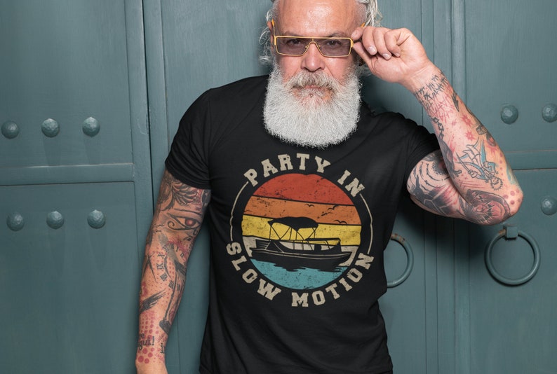 K&ouml;nnte beinhalten: Ein schwarzes T-Shirt mit einer Grafik im Vintage-Stil eines Bootes auf dem Wasser mit dem Text "Party in Slow Motion".