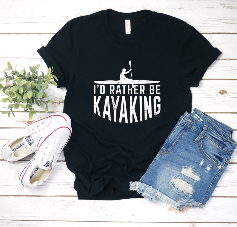 May include: A black t-shirt with a white graphic of a person kayaking and the text "I'd rather be kayaking".