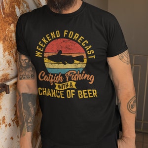 May include: Black t-shirt with a vintage-style graphic that says "Weekend Forecast Catfish Fishing with a Chance of Beer". The graphic features a catfish and a sunset.
