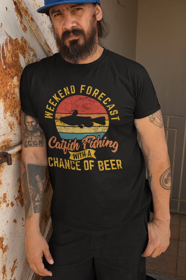 May include: Black t-shirt with a vintage-style graphic that says "Weekend Forecast Catfish Fishing with a Chance of Beer". The graphic features a catfish and a sunset.