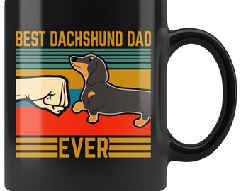 May include: Black ceramic mug with the text "BEST DACHSHUND DAD EVER" in a retro design. The mug features a cartoon dachshund and a fist bump graphic in a colorful, horizontal striped background.