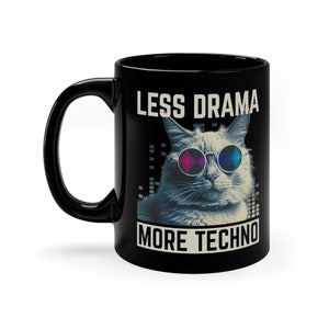 Op de afbeelding: Zwarte keramische koffiemok met een witte kat die een zonnebril draagt en een geluidsgolfgrafiek. De tekst "Less Drama More Techno" is op de mok gedrukt.