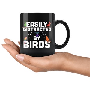 Puede incluir: Taza de cer&aacute;mica negra con el texto blanco &laquo;EASILY DISTRACTED BY BIRDS&raquo;. La taza presenta ilustraciones coloridas de varias aves, como un loro, un colibr&iacute; y un cardenal. La taza tiene un asa grande.