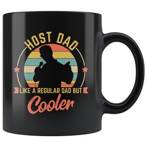 Pode incluir: Caneca de cerâmica preta com um design gráfico branco que diz "Host Dad Like a Regular Dad But Cooler" com um gráfico de pôr do sol de estilo retrô e uma silhueta de uma pessoa segurando um microfone.