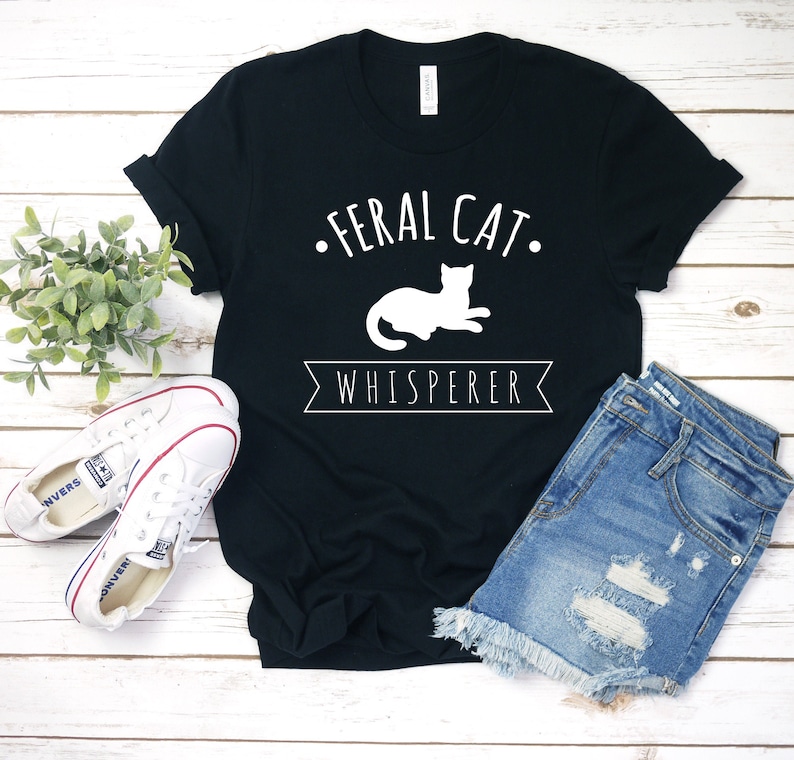 May include: Black t-shirt with white text that reads "Feral Cat Whisperer" and a silhouette of a cat.