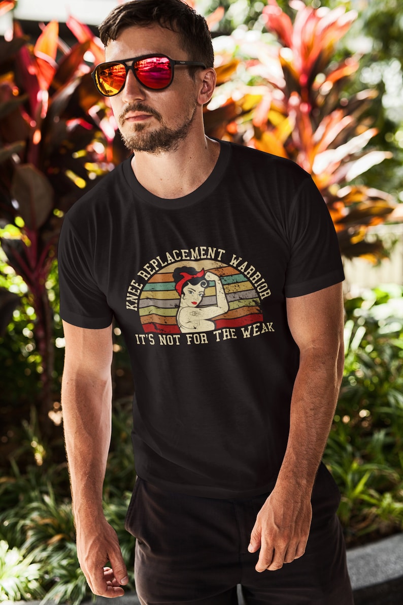 May include: A black t-shirt with a vintage-style graphic of a woman flexing her bicep. The graphic says "Knee Replacement Warrior" and "It's not for the weak".