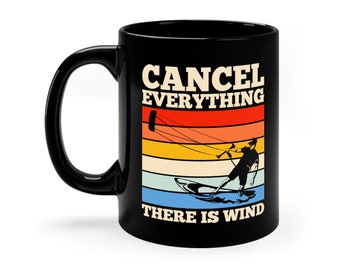 May include: Black coffee mug featuring a retro-style graphic of a person kitesurfing. The text on the mug reads "Cancel Everything There Is Wind".