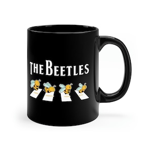 May include: Black coffee mug with a white graphic of four bees walking across a crosswalk with the text "THE BEETLES" above them.