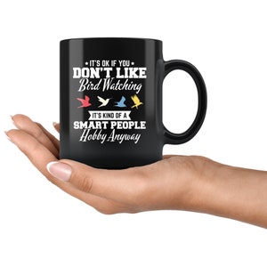 May include: Black ceramic mug with a white graphic that reads "IT'S OK IF YOU DON'T LIKE Bird Watching. IT'S KIND OF A SMART PEOPLE Hobby Anyway." The design includes three colorful bird silhouettes. The mug has a large handle.