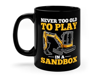 May include: Black coffee mug featuring a yellow excavator graphic and the text "Never too old to play in a sandbox".