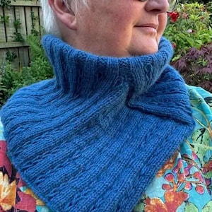 May include: A vibrant blue knitted cowl with a ribbed texture. The cowl is a neck warmer with a high, folded collar. The text "LinkedIn cowl" is displayed at the bottom. The cowl is made of a soft, textured yarn.