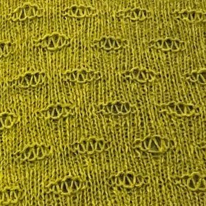 May include: A close-up of a yellow knitted fabric with a textured pattern. The fabric has a woven design with small holes throughout.