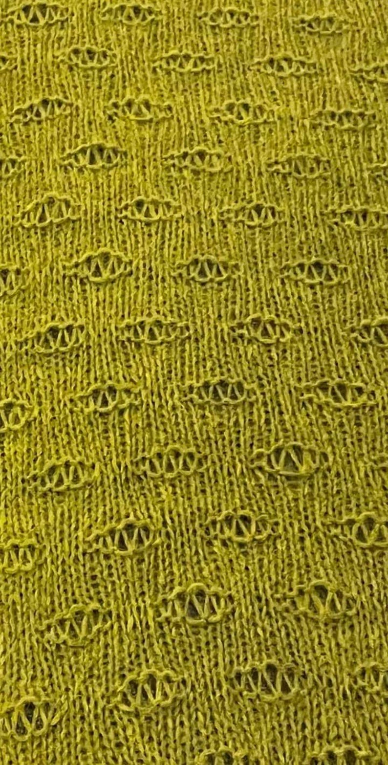 May include: A close-up of a yellow knitted fabric with a textured pattern. The fabric has a woven design with small holes throughout.