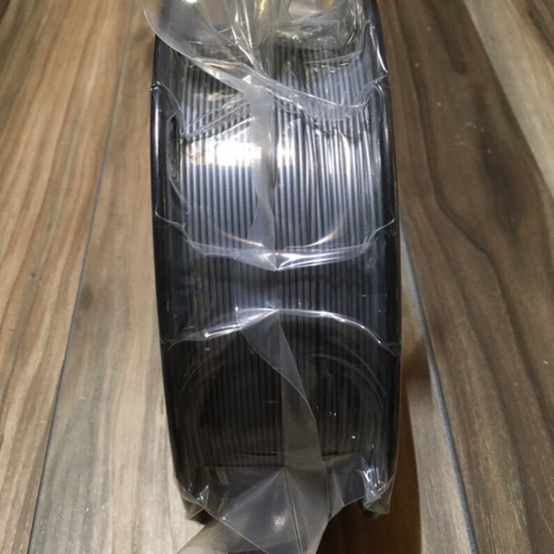 May include: A spool of black filament for 3D printing, wrapped in clear plastic.