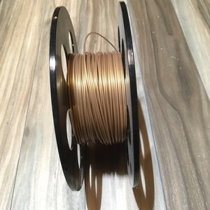 May include: A spool of gold-colored filament for a 3D printer.