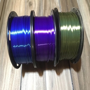 May include: Three spools of filament for 3D printing. The filament is blue, purple, and green.