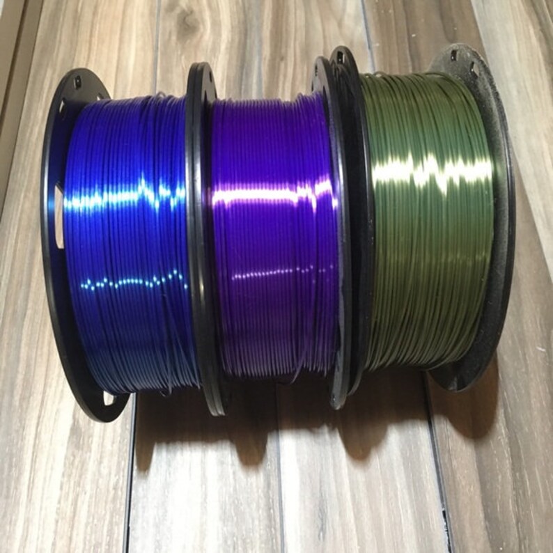 May include: Three spools of filament for 3D printing. The filament is blue, purple, and green.