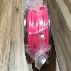 May include: A spool of bright pink filament for 3D printing, wrapped in clear plastic and secured with a ribbon.
