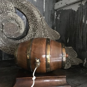 May include: A small wooden barrel with brass bands and a spigot, mounted on a wooden base. The barrel is brown and the base is dark brown.