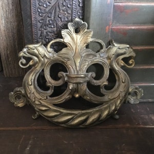 May include: Ornate brass door knocker with a decorative design featuring two stylized animal heads and a central floral motif.