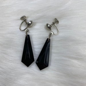 May include: A pair of black, geometric shaped dangle earrings with silver clip-on backs.