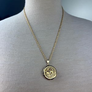 May include: A gold chain necklace with a round pendant featuring a detailed floral design.