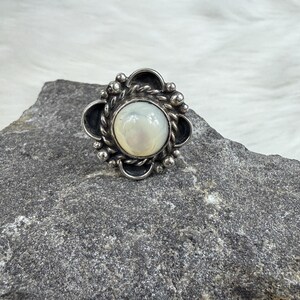 May include: A silver ring with a white mother-of-pearl stone set in a floral design.