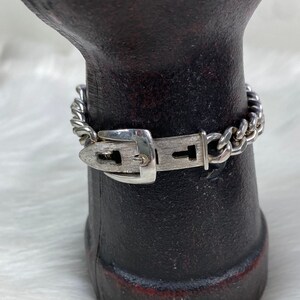 May include: A silver bracelet with a buckle clasp. The bracelet is made of a chain link design.