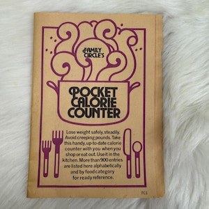 May include: A brown booklet with a purple illustration of a pot with steam coming out of it. The text on the cover reads "Family Circle's Pocket Calorie Counter". The text below the illustration reads "Lose weight safely, steadily. Avoid creeping pounds. Take this handy, up-to-date calorie counter with you when you shop or eat out. Use it in the kitchen. More than 900 entries are listed here alphabetically and by food category for ready reference."