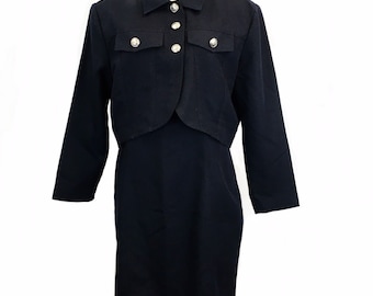 May include: A black dress with a matching cropped jacket. The jacket has a collar and silver buttons. The dress has a fitted silhouette.