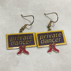 May include: A pair of gold earrings with a purple and yellow sign that says "private dancer" and red shoes hanging from the bottom.