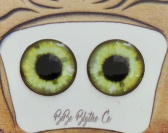 May include: A pair of green and black doll eyes with a white background. The eyes are displayed in a gift box with a bow on top. The box has the text "Bye Bye Blythe Co." printed on the bottom.