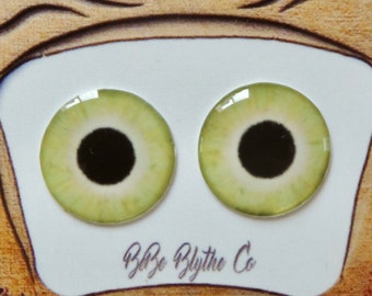 Puede incluir: Un par de ojos de muñeca Blythe verdes con pupilas negras e iris blancos, mostrados sobre un fondo blanco con un marco de madera marrón y el texto "Blye Blythe Co."