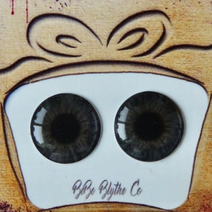 May include: A pair of gray Blythe doll eyes with black pupils, displayed in a white box with a brown ribbon and the text "Blythe Blythe Co."