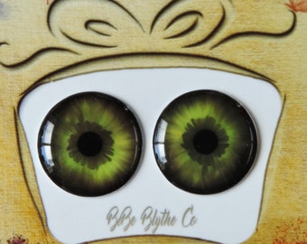 Puede incluir: Un par de ojos de muñeca Blythe verdes y negros con una pupila negra y un iris verde. Los ojos se muestran sobre un fondo blanco con un marco de madera marrón y el texto "B&B Blythe Co."