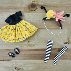 May include: A yellow and black bee-themed dress with black sleeves, a pair of black shoes, a black and white striped pair of stockings, and a headband with yellow and pink felt flowers.
