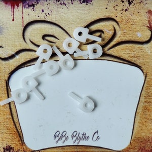 May include: A close-up of a white gift box with a brown and white painted background. The box is decorated with a white ribbon and bow. The box is filled with small white plastic pieces. The text "Blythe Blythe Co" is written on the box.