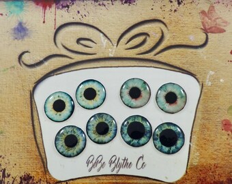 May include: A set of eight doll eyes with different color patterns, including blue, green, and brown. The eyes are arranged in a circle on a white background with the text "B&B Blythe Co." at the bottom.