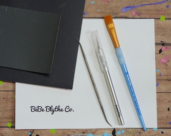 May include: A set of craft supplies for creating miniature doll accessories, including a piece of sandpaper, a small metal file, a craft knife, and a paintbrush. The supplies are laid out on a white surface with the text "BeBe Blythe Co."