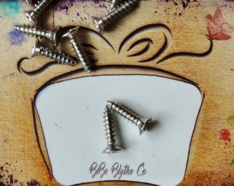 May include: A close-up of a small white card with the text "By: Blythe Co." printed on it. The card is surrounded by a scattering of silver screws on a brown background with colorful paint splatters.