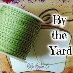 May include: A spool of green thread with the text "By the Yard" on a brown background.