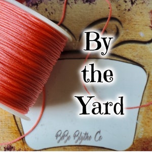 Puede incluir: Una bobina de cordón de color coral con el texto "By the Yard" en una etiqueta blanca.