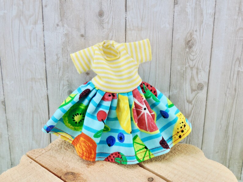 May include: A blue and yellow striped dress with a fruit print skirt. The skirt features a variety of fruits, including lemons, oranges, strawberries, and blueberries.