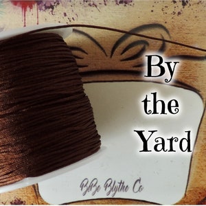 May include: A spool of brown cord with the text "By the Yard" and "Blythe Blythe Co." on a white label.