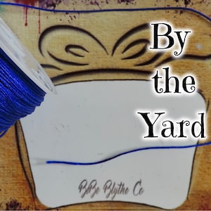 May include: A spool of royal blue cord with a white label that says "By the Yard".