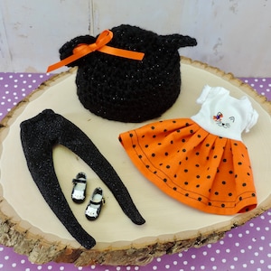 May include: A black crocheted witch hat with an orange ribbon, a black pair of leggings, a pair of black shoes, and a white dress with orange polka dots and a cat face design.