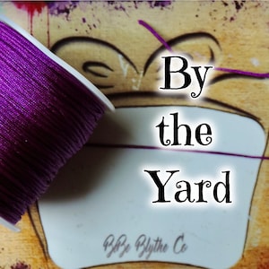 May include: A spool of purple thread with the text "By the Yard" and "By Blythe Co" on a white label.