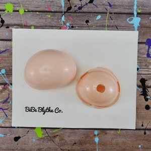 Peut inclure: Deux moitiés d'un moule de tête de poupée en plastique rose. Le moule est conçu pour créer des têtes de poupée Blythe. Le moule est sur une surface blanche avec le texte "BeBe Blythe Co." imprimé dessus.