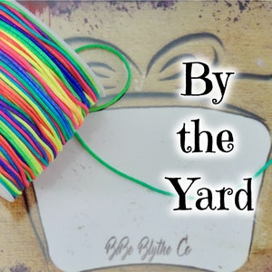 May include: A spool of colorful waxed cord with a green cord extending from it. The text "By the Yard" is written on a white background.